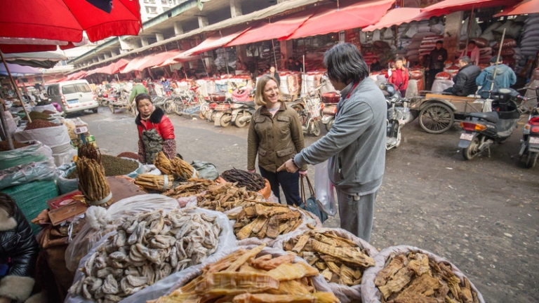 Foreign traveler smiling and talking with a local person at a street market in China showing friendly and safe travel experience