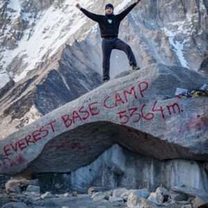 Climber on rock with Everest Base Camp sign at 5364m.