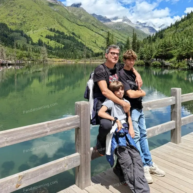 A father walking with his two sons at a wooden railing overlooking mountains in Western Sichuan