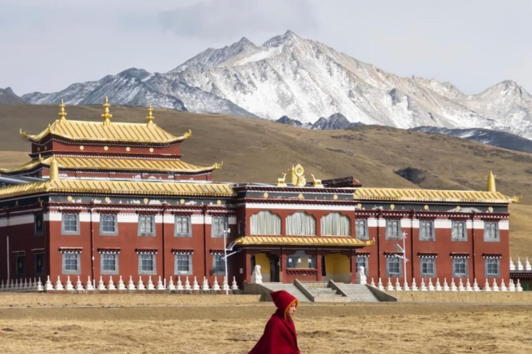 Monk walking past Muya Monastery with snow mountains in the background
