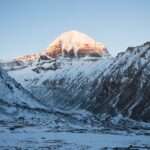 A majestic view of Mount Kailash with snow-covered terrain and a bright sunrise.